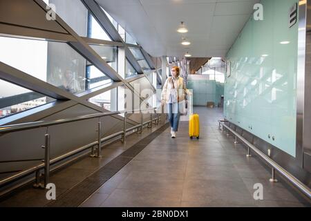 Passagierin Frau mit einer medizinischen Schutzmaske zur Verhinderung Coronavirus zu Fuß mit ihrem Gepäck in fast Flughafen / Reisestation. Reise BA Stockfoto