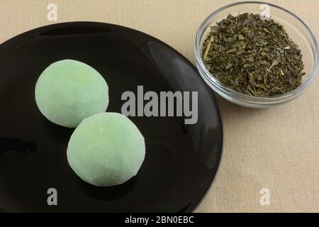 Grüner Tee Eis Mochi Kugeln auf schwarzem Dessertteller mit grünem Tee in Glasschüssel auf brauner Tischdecke Stockfoto