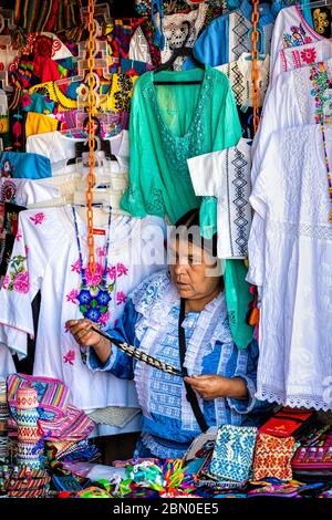 Eine Verkäuferin, die von ihren Waren umgeben ist, auf dem Kunsthandwerksmarkt von Valle de Bravo im mexikanischen Bundesstaat Mexiko. Stockfoto