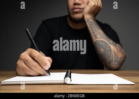 Asian Mann Schreiben auf einem Notizbuch mit langweiligen Gesicht auf Holztisch. Konzept über Remote-Arbeit. Stockfoto
