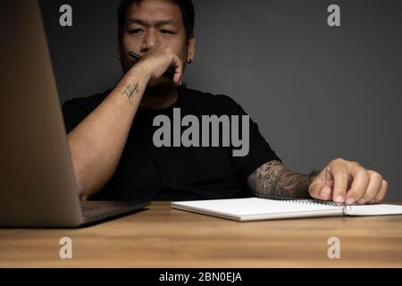 Asian Mann Blick auf Monitor mit Fokussierung Gesicht auf Holztisch mit Laptop. Konzept über Remote-Arbeit. Stockfoto