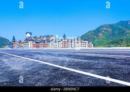 Die leere autofreie Autobahn und das im europäischen Stil erbaute Schloss, in der Ferne grüne Berge. Stockfoto