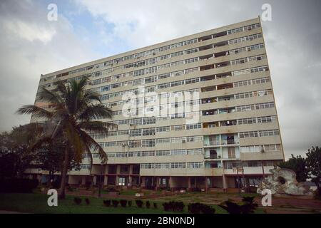 Großes altes Appartementhaus / Gebäude typisch für kommunistische Ära mit tropischen Kokospalmen davor in einer armen Nachbarschaft / Straße in Vedado Distri Stockfoto