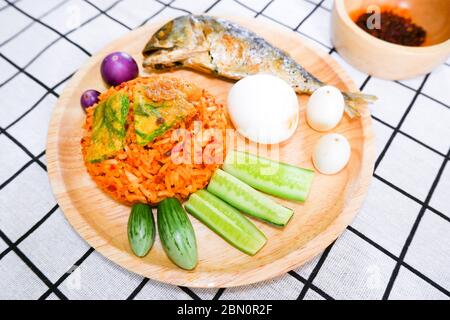 Gebratener Reis mit Prik pao (Chili Paste mit Sojaöl), Omelette mit Cha om, gekochtes Hühnerei, Gurke, Aubergine und gebratene Makrele in Holzpl Stockfoto