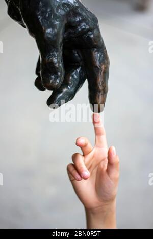 Eine menschliche Hand berührt Finger an Finger mit einer Statue wie Michelangelo und seinem berühmten Gemälde von Gott und Mensch Schöpfung Stockfoto