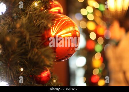 Nahaufnahme einer roten Kugel, die von einem geschmückten Weihnachtsbaum hängt. Retro-Filtereffekt. Bokeh Stockfoto