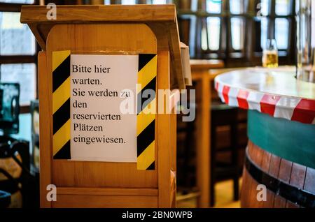 Mainz, Deutschland. Mai 2020. An einem Stehpult mit der Notiz 'Bitte warten Sie hier. Sie werden zu den reservierten Plätzen geführt. Die Gäste des traditionellen Pubs zur Andau werden begrüßt. Die Taverne im Stadtzentrum will unter Einhaltung der Corona Hygienevorschriften wieder eröffnet werden. Die Landesregierung in Rheinland-Pfalz hat zum 13. Mai grünes Licht für die Gastronomie gegeben. Quelle: Andreas Arnold/dpa/Alamy Live News Stockfoto