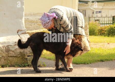 Eine alte Frau streichelte und kümmert sich um einen obdachlosen Hund in der Nähe der Kirche Stockfoto