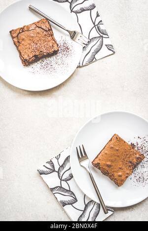 Draufsicht auf zwei Dessertteller mit Brownie-Kuchen auf weißem rustikalem Hintergrund.