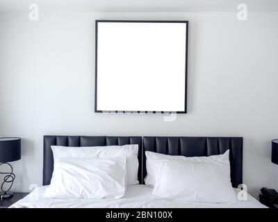 Leeres Foto quadratischen Rahmen Mockup auf weißer Wand über dem Bett mit weißen sauberen Kissen im Schlafzimmer. Stockfoto