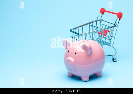 Rosa Sparschwein und Warenkorb auf blauem Hintergrund. Das Konzept, Geld beim Einkaufen im Geschäft zu sparen. Stockfoto