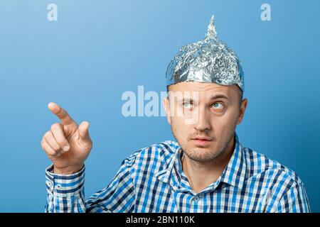 Folienhut auf Mann. Mann mit einem überraschten Gesicht zeigt Daumen nach oben. Schützt vor dem Lesen denken. Stockfoto