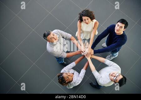 Ein multiethnisches Team von Geschäftsleuten, die sich die Hände stapeln und in der Kamera nach oben schauen, Ansicht von oben Stockfoto