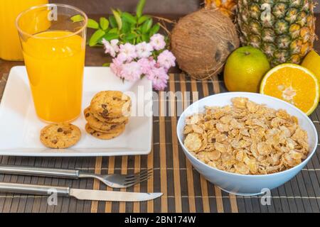 Frühstück, das Milch in Cornflakes gießt, wodurch Apfelsplash und Orangenobst-Kekse entstehen Stockfoto