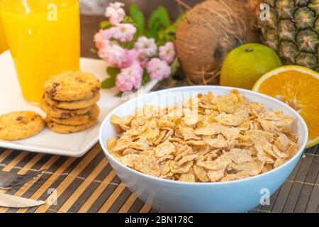 Frühstück, das Milch in Cornflakes gießt, wodurch Apfelsplash und Orangenobst-Kekse entstehen Stockfoto