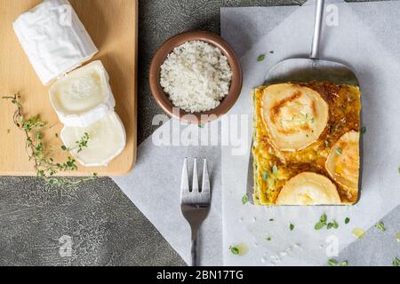 Zucchini Pie oder Quiche mit Ziegenkäse auf Holzbrett. Scheibe Ziegenkäse in der Nähe. Gesunde vegetarische Speisen, Mittag- oder Abendessen. Draufsicht. Stockfoto