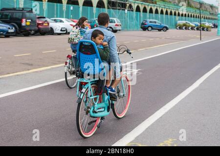 Kinder, die in Großbritannien auf einem Kindersitz auf der Rückseite eines Fahrrads fahren, ohne einen Sicherheitshelm zu tragen. Stockfoto