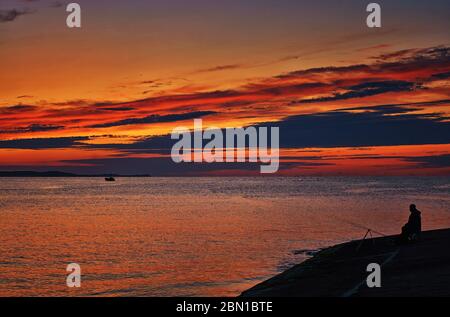 Angler auf dem Ostseestaum im Sonnenuntergang mit orangefarbenem Himmel. Stockfoto