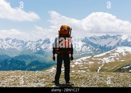 Rückansicht eines Mannes touristischer Bergsteiger in Sportbekleidung und großem Rucksack steht auf dem Gipfel des Berges und bewundert malerische Aussicht auf Tal und Berg Stockfoto