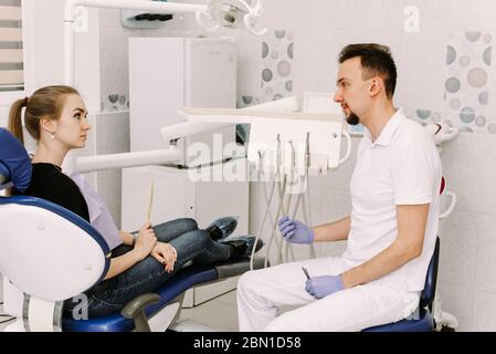 Ein schönes Mädchen sitzt im Zahnarztstuhl und hört dem Arzt zu. Zahnarzt Termin und zahnärztliche Versorgung. Stockfoto