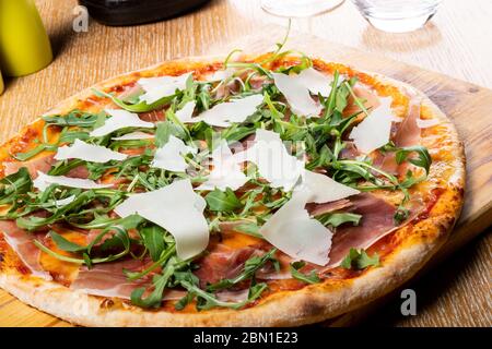 Frisch gebackene traditionelle Prosciutto, Rucola, Tomaten und Parmesan Pizza, serviert auf einem Holzbrett Stockfoto