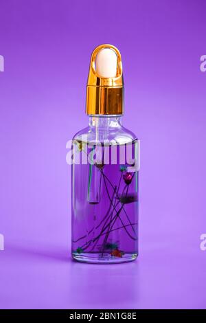 Tropfflasche Flasche mit Blumen innen Mock-up. Kosmetische Pipette auf violettem Hintergrund. Nagelhautöl Stockfoto