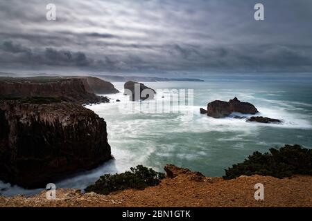 Landschaftlich reizvolle Aussicht auf die Küste entlang Carrapateira mit den Felsformationen und Wellen, die bei einem Sturm zusammenbrechen, in Algarve, Portugal Stockfoto