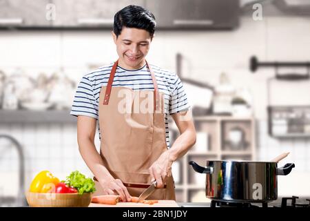 Asian Mann schneiden Gemüse mit einem Messer auf Schneidebrett in der Küche Zimmer Stockfoto