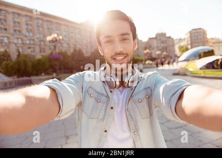 Selfie-Manie! Aufgeregt junger Kerl macht Selfie auf einer Kamera. Er trägt lässige trendige Kleidung und große Kopfhörer, auf einem Spaziergang in der Stadt draußen Stockfoto