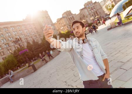 Selfie-Zeit! Junge funky Blogger macht Foto für seine Social-Networks-Seite, er posiert in einem lässigen Outfit und Kopfhörer, auf der Straße in der Stadt Stockfoto