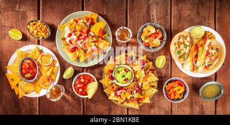 Mexikanisches Speisepanorama, aufgenommen von oben auf einem dunklen rustikalen Holzhintergrund. Nachos, Guacamole, Tequila, Tacos, ein flacher Lay Stockfoto