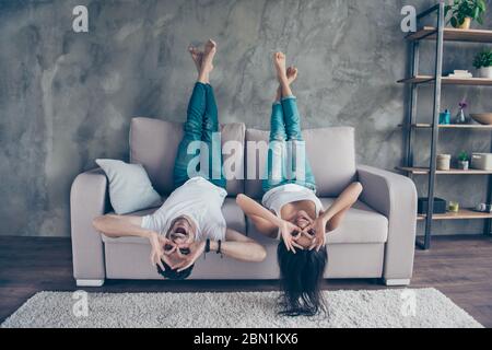 Lustige Paare mit Brille Gesturing liegen umgedreht auf dem Sofa zu Hause. Sie sind so fröhlich, haben Spaß zusammen, gehen verrückt, Bruder und Schwester Stockfoto