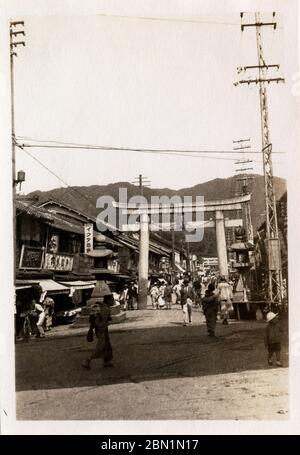 [ 1930er Jahre Japan - Sacred Torii Gate in Shopping Street in Kobe ] - Steinlaternen und ein verängstigter Torii-Tor am Eingang zum Ikuta Jinja, einem schintoistischen Schrein in Kobe, Präfektur Hyogo, Ca 1932 (Showa 7). Viele Geschäfte säumen die Straße. Der Schrein gehört zu den ältesten Schreinen in Japan und wird im Nihon Shoki, dem zweitältesten Buch der klassischen japanischen Geschichte, erwähnt. Die Schlacht von Ichi-no-Tani (1184) fand im und um den Ikuta-Schrein statt. Silberdruck mit Gelatine aus dem 20. Jahrhundert. Stockfoto