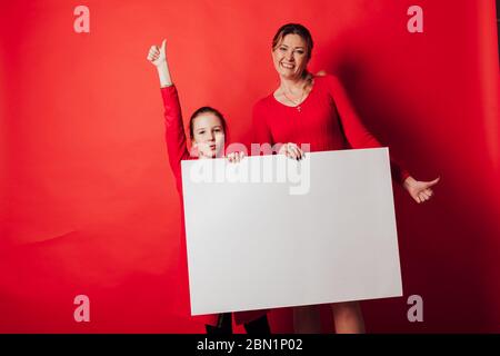 Mädchen und Frau hält ein Schild für Inschriften auf rotem Hintergrund Stockfoto