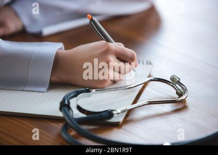 Nahaufnahme von Arzthände mit Stethoskop, weißen Laken und Pillen auf Holztisch Hintergrund. Arzt während seiner Arbeit mit Patienten, erklären Rezepte für Medikamente, Beratung, Behandlung. Stockfoto