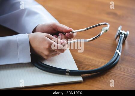 Nahaufnahme von Arzthände mit Stethoskop, weißen Laken und Pillen auf Holztisch Hintergrund. Arzt während seiner Arbeit mit Patienten, erklären Rezepte für Medikamente, Beratung, Behandlung. Stockfoto
