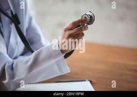Nahaufnahme von Arzthände mit Stethoskop, weißen Laken und Pillen auf Holztisch Hintergrund. Arzt während seiner Arbeit mit Patienten, erklären Rezepte für Medikamente, Beratung, Behandlung. Stockfoto