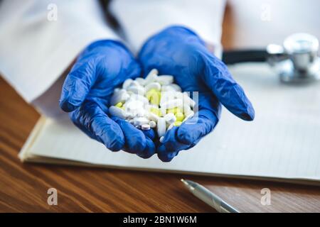 Nahaufnahme von Arzthände mit blauen Schutzhandschuhen auf Holztischhintergrund. Geben von Pillen. Arzt während seiner Arbeit mit Patienten, erklären Rezepte für Medikamente, Beratung, Behandlung. Stockfoto