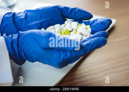 Nahaufnahme von Arzthände mit blauen Schutzhandschuhen auf Holztischhintergrund. Geben von Pillen. Arzt während seiner Arbeit mit Patienten, erklären Rezepte für Medikamente, Beratung, Behandlung. Stockfoto