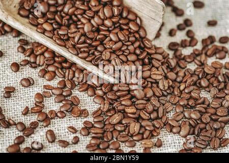 Holzschaufel mit gerösteten Kaffeebohnen Nahaufnahme auf Hintergrund auf Sacktuch, selektiver Fokus, Vintage-Hintergrund Stockfoto