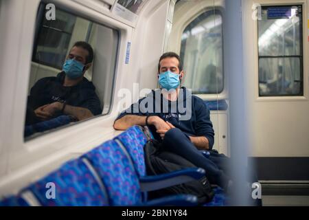 Ein Passagier, der eine Gesichtsmaske trägt, schließt seine Augen auf der Jubilee Line im Zentrum Londons während der üblichen Morgenverkehrszeit. Stockfoto