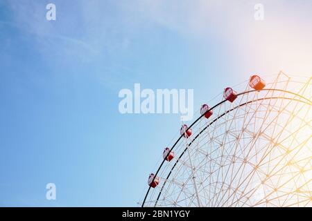 Riesenrad mit leuchtend roten Ständen auf Hintergrund von heiterem klaren blauen Himmel mit Sonnenflammen als Symbol der Freude Erholung Entspannung Spaß und gute Zeit, Witz Stockfoto