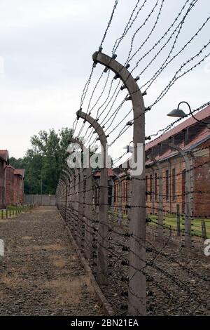 Auschwitz Holocaust Memorial Museum - Blick entlang elektrischer Stacheldrahtzaun mit Häftlingsbaracken im Hintergrund Stockfoto