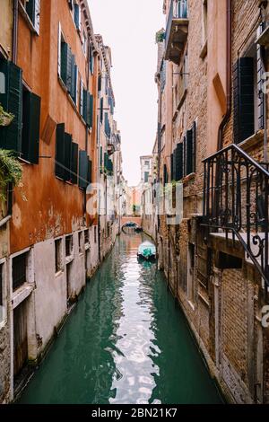 Schöner schmaler Kanal in Venedig, Italien. Zwischen zwei Gebäuden. Eine kleine Brücke in der Ferne. Boot vor der Wand des Hauses. Links Stockfoto