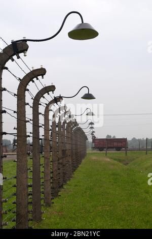 Auschwitz Holocaust Memorial Museum - Blick entlang elektrischen Stacheldrahtzaun mit Schienenwagen im Hintergrund für den Transport verwendet Stockfoto