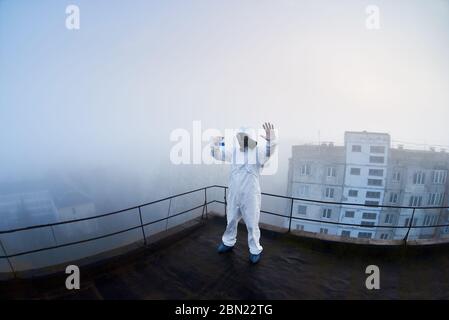 Fischaugen-Schnappschuss eines Mannes in einer schützenden Schutzhülle und Gasmaske, der in einer potenziell gefährlichen Ausschlusszone arbeitet und ein Stoppschild in Quarantäne gestiert Stockfoto