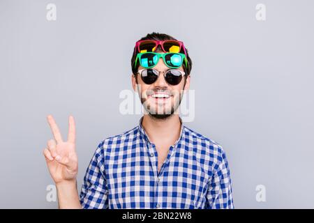 Cool! Verspielt junge Brünette bärtigen Mann in drei Paar helle bunte Gläser und karierte casual Shirt ist töricht herum, posiert und zeigt V Stockfoto