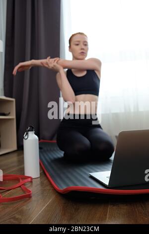 Das Mädchen ist in Stretching engagiert, Blick auf den Laptop vor ihr, den Fokus auf das elastische Band. Stockfoto