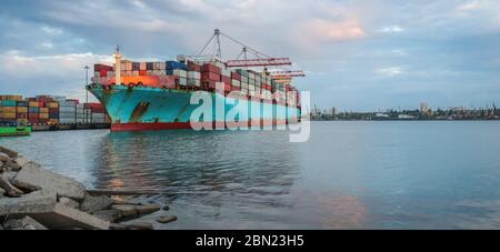 Containerfrachtschiffladung im Seehafen bei Dämmerung. Logistik und Transport von Container Cargo Schiff mit funktionstüchtigen Kranbrücke in der Werft, Logistik Stockfoto