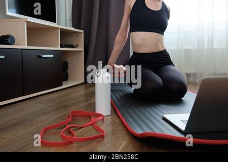 Das Mädchen ist in Stretching vor dem Laptop engagiert, die Fokus Sportflasche in der Nähe. Stockfoto